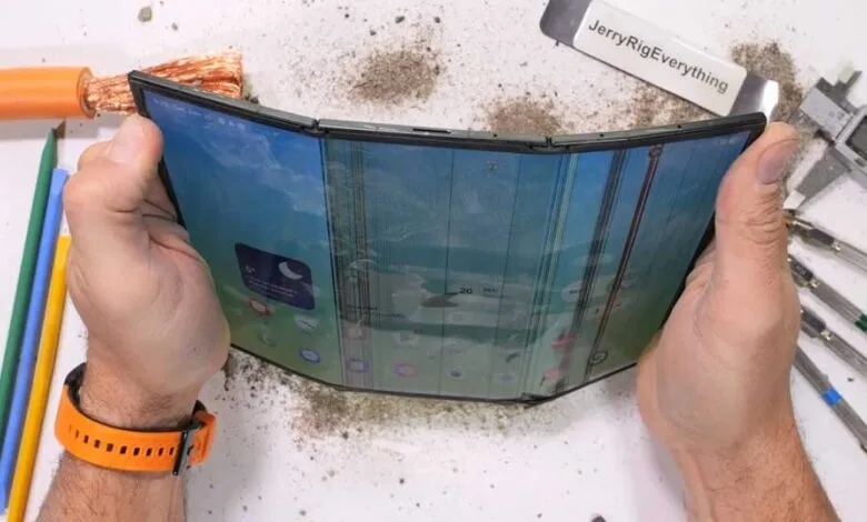 Hands holding a damaged, tri-fold smartphone with a cracked screen.
