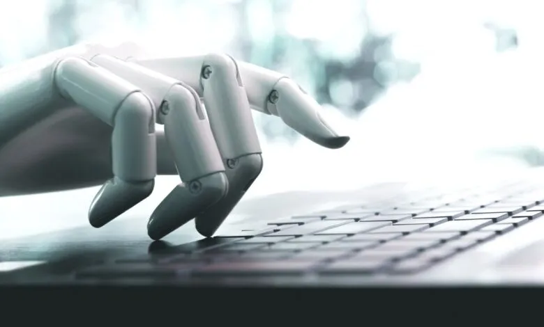 Close-up of a robotic hand typing on a laptop keyboard.