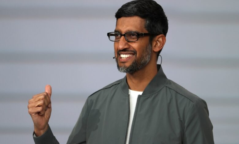 Sundar Pichai smiles, giving a thumbs up, wearing glasses and a gray jacket.