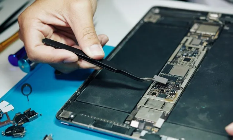 Close-up of hands repairing an open tablet with tweezers.