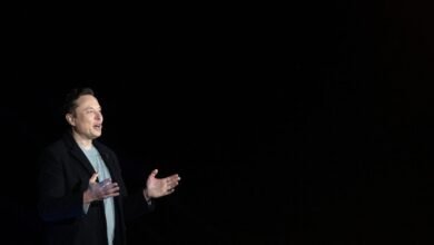 Elon Musk gesturing on stage against a dark background.