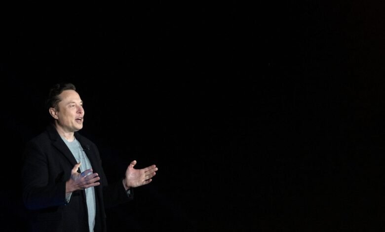 Elon Musk gesturing on stage against a dark background.