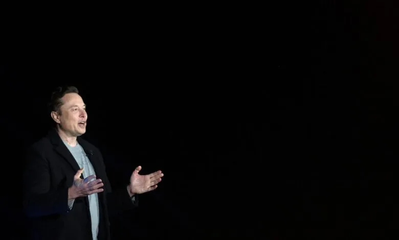 Elon Musk gesturing on stage against a dark background.