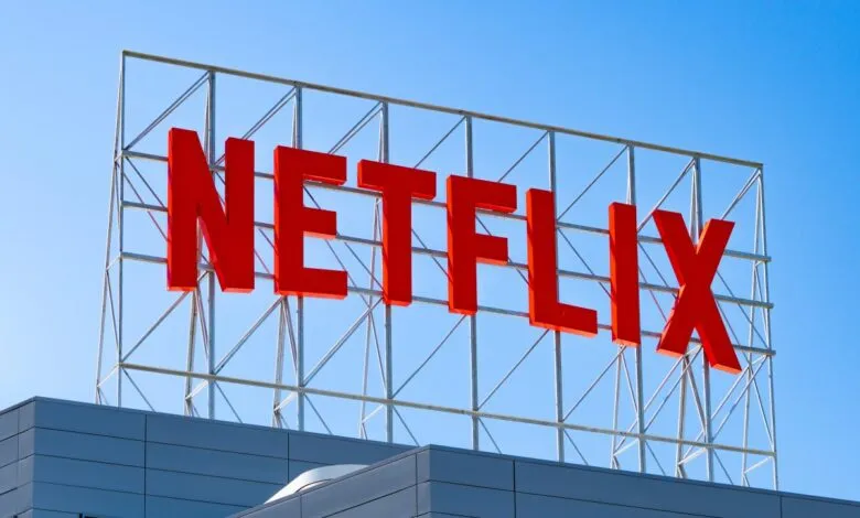 Large red Netflix logo on a silver metal frame against a clear blue sky.