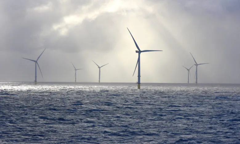 Offshore wind farm with multiple turbines in the sea under a cloudy sky with sunbeams.