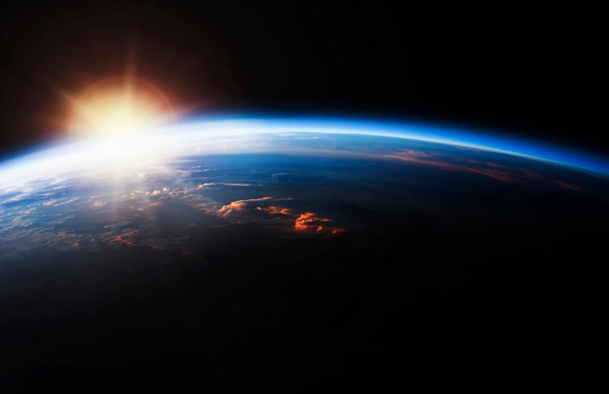 Earth from space with sunrise, showing atmosphere and cloud formations.