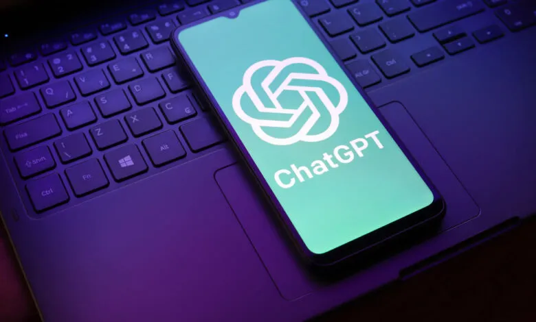Smartphone displays the ChatGPT logo on a laptop keyboard, illuminated in purple light.