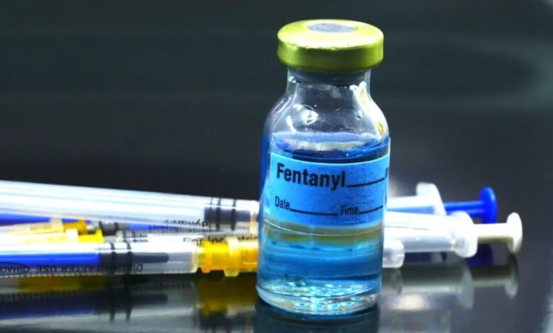 Vial of Fentanyl with syringes on a dark, reflective surface.