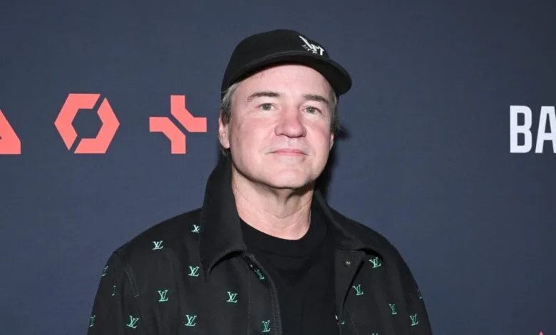 Actor Dylan McDermott poses at an event, wearing a black cap and patterned jacket.