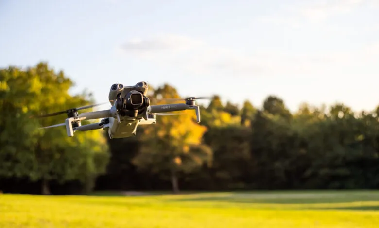 DJI Mini 5 Pro drone hovering over a grassy field with trees in the background.