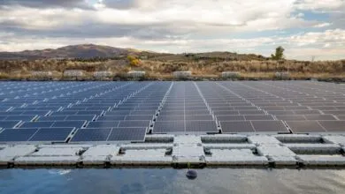 Floating solar panels on a pond with hills and cloudy sky in the background.