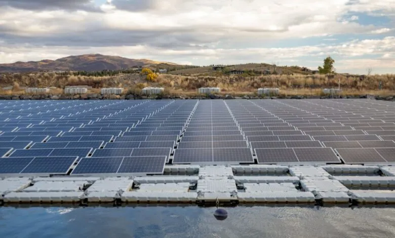 Floating solar panels on a pond with hills and cloudy sky in the background.