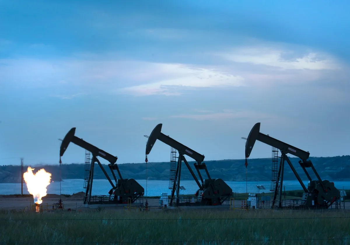 Three pump jacks silhouetted against a blue sky with a gas flare.