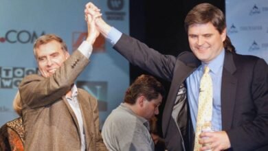 Two men in suits high-fiving on stage in front of company logos.