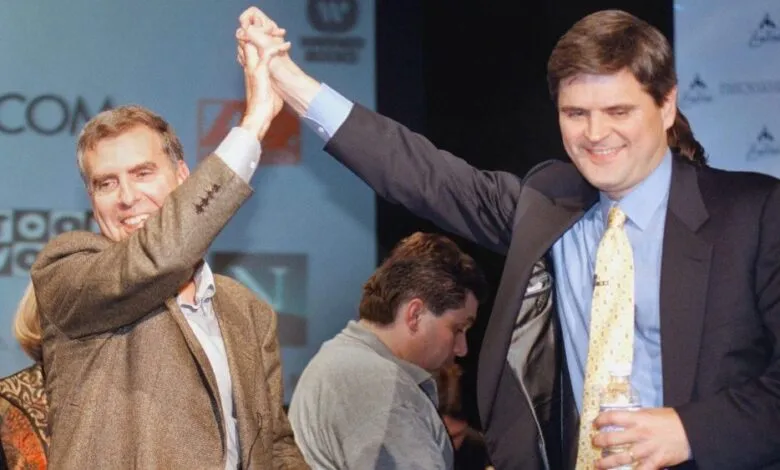 Two men in suits high-fiving on stage in front of company logos.