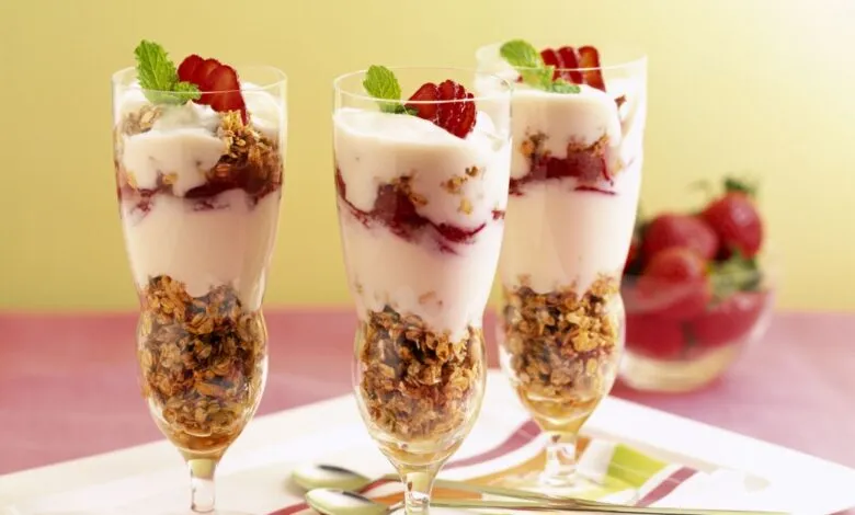 Three parfait glasses filled with yogurt, granola, strawberries, and mint.