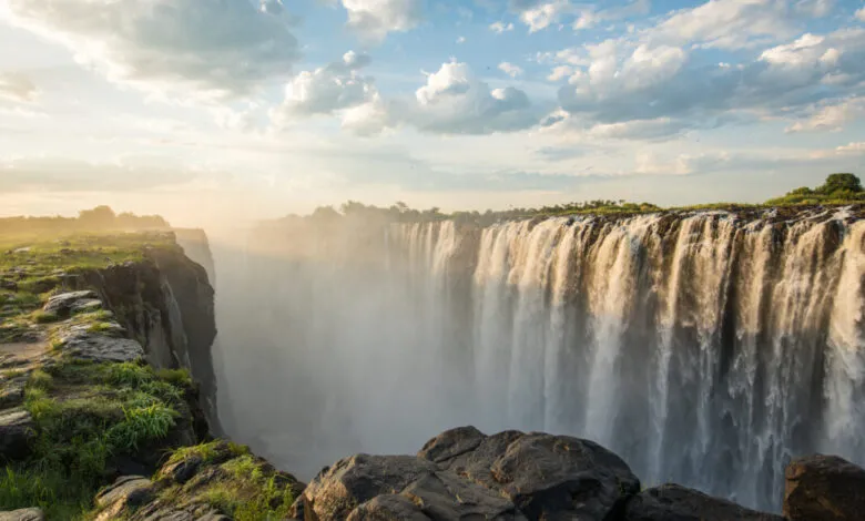 Victoria Falls plunges into mist-filled gorge under cloudy sky.