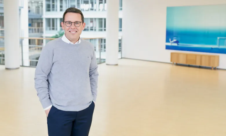 Man in gray sweater and glasses smiles in modern office space.