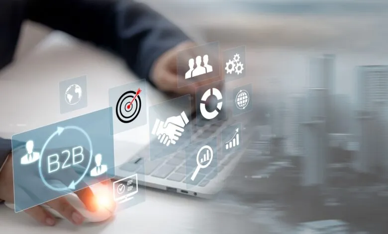 Hand using mouse with B2B and business icons overlaid on a laptop.