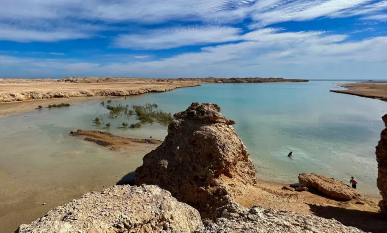 Scenic view of turquoise water, sandy beach, and rocky formations under a blue sky.