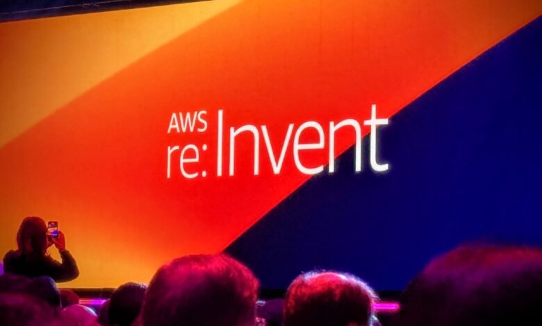 Audience views AWS re:Invent conference stage with bright orange and blue backdrop.