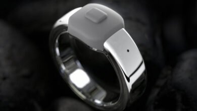 Silver smart ring with gray button on dark textured background.