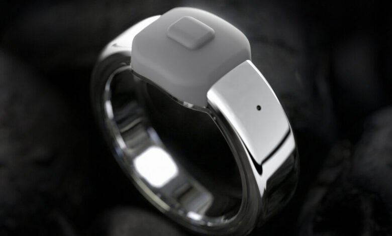 Silver smart ring with gray button on dark textured background.