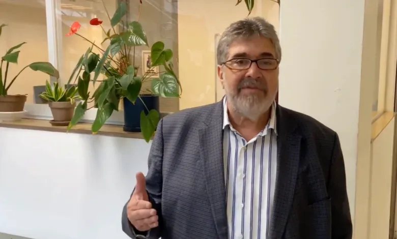 Man with glasses and beard gives a thumbs up in an office setting.