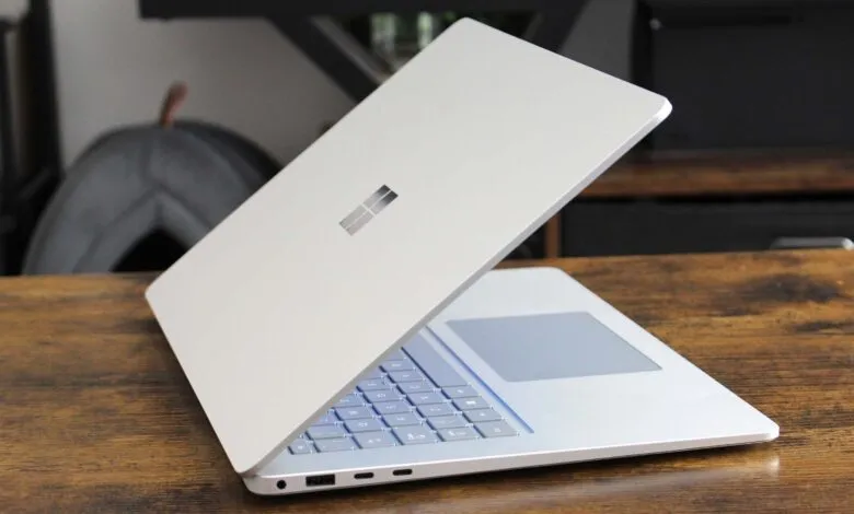 Silver Microsoft Surface Laptop partially open on a wooden table.