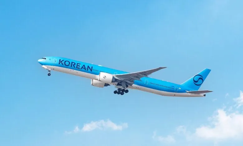 Korean Air plane ascends against a clear blue sky, landing gear visible.