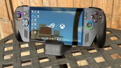 ROG Ally handheld gaming console on a stand, screen displaying Windows desktop.