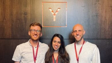 Three smiling people stand in front of a wall with a 'Y' logo.