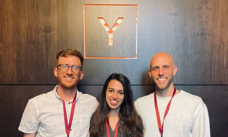 Three smiling people stand in front of a wall with a 'Y' logo.