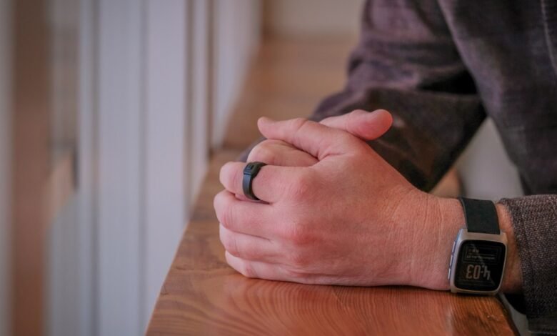 Person's hands with smart ring and watch resting on wooden surface.