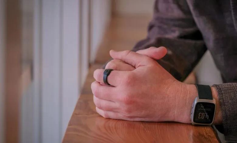 Person's hands with smart ring and watch resting on wooden surface.