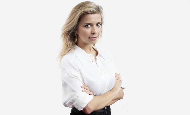 Portrait of a blonde woman with arms crossed, wearing a white shirt.