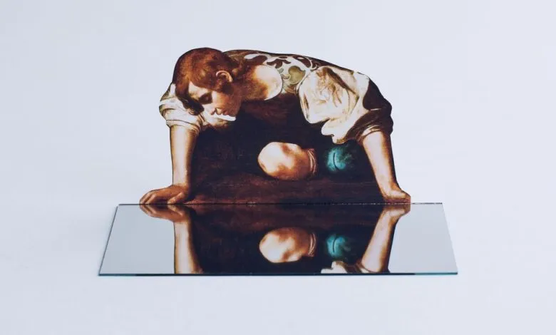 Cutout of a figure from a painting reflected in a mirror on a white surface.