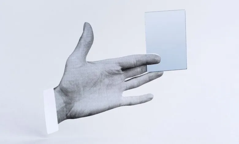Monochrome hand holding a reflective card against a white background.