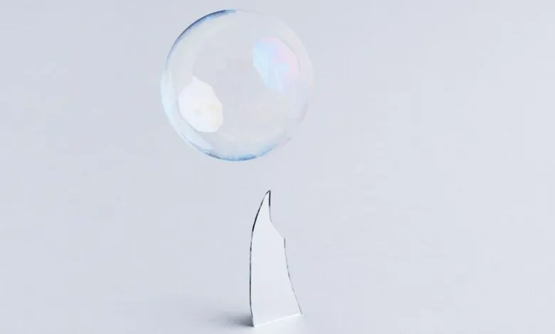 Soap bubble hovers above a shard of glass on a white surface.
