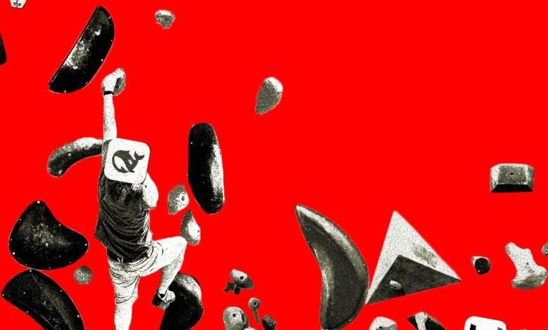 Person climbing a red rock wall with various handholds and a logo on their back.