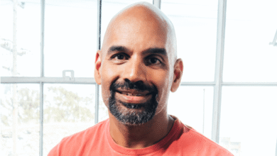 Headshot of a smiling man with a beard in front of a window.