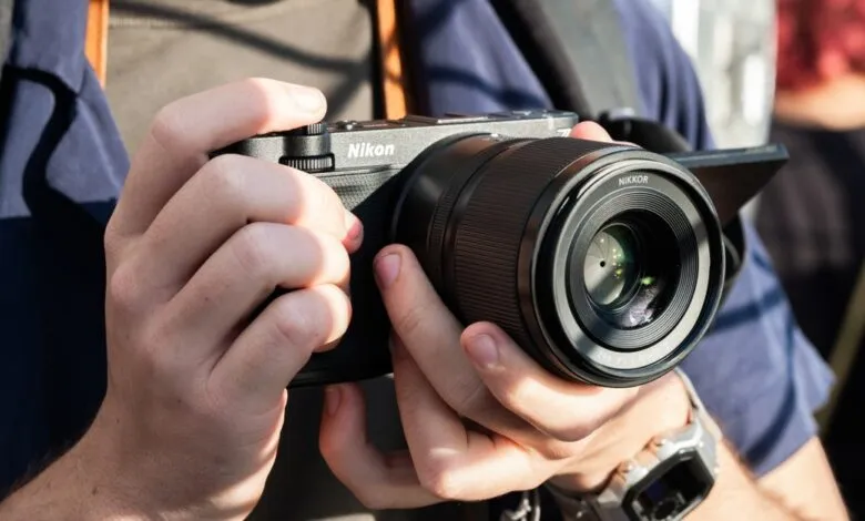 Close-up of a person holding a black Nikon camera with a Nikkor lens.