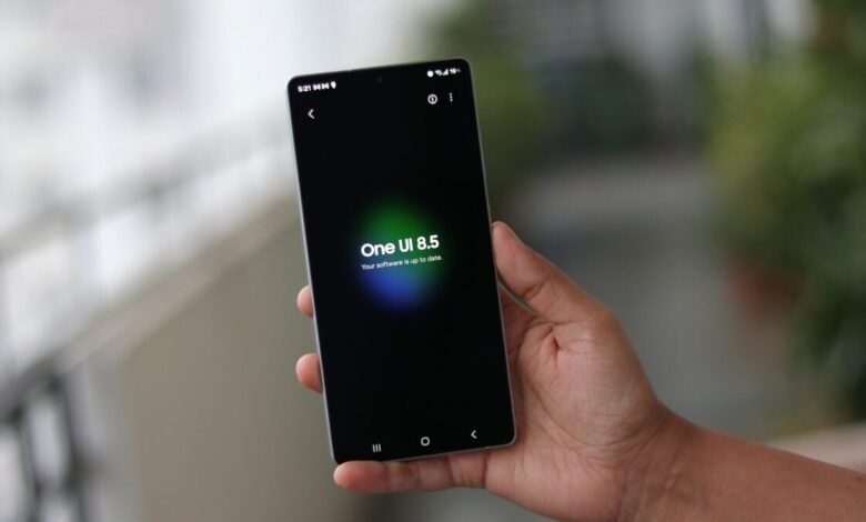 Hand holding a smartphone displaying 'One UI 8.5' software update message.