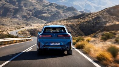 Blue BMW iX3 driving on a winding road through a mountainous landscape.