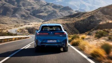 Blue BMW iX3 driving on a winding road through a mountainous landscape.