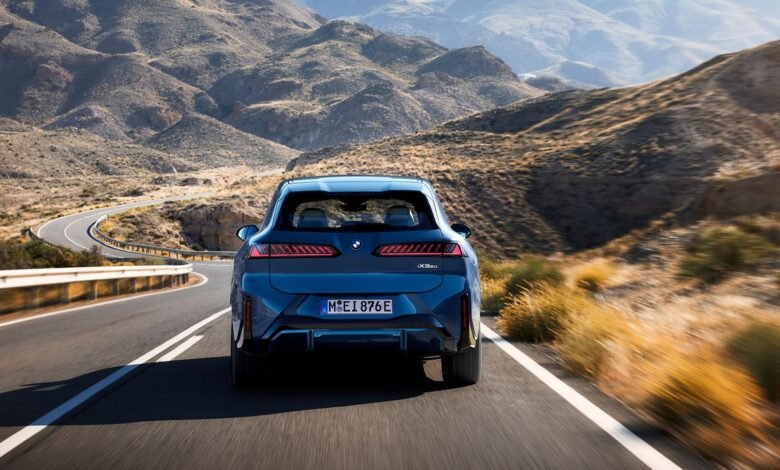 Blue BMW iX3 driving on a winding road through a mountainous landscape.