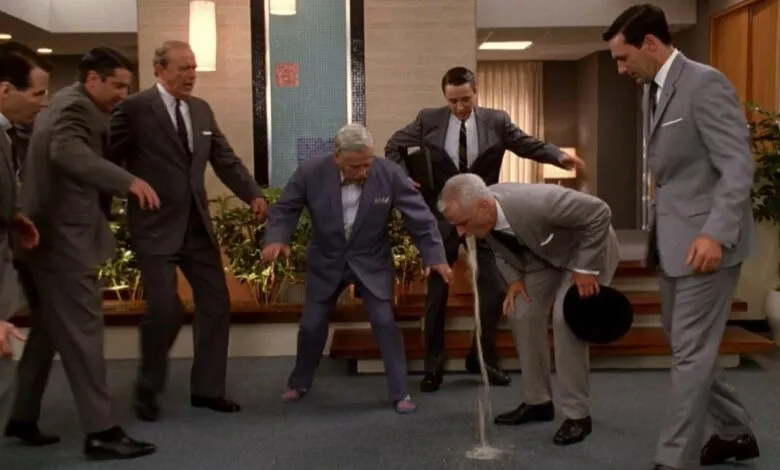 Scene from Mad Men: Roger Sterling vomits in office surrounded by colleagues.