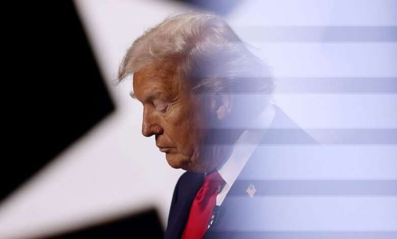 Donald Trump with head bowed, wearing suit and American flag pin.