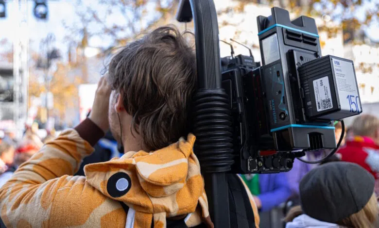 Cameraman in giraffe costume carries Haivision camera rig at outdoor event.