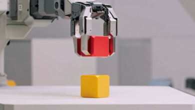 Robotic arm holding red cube above yellow cube on white surface.